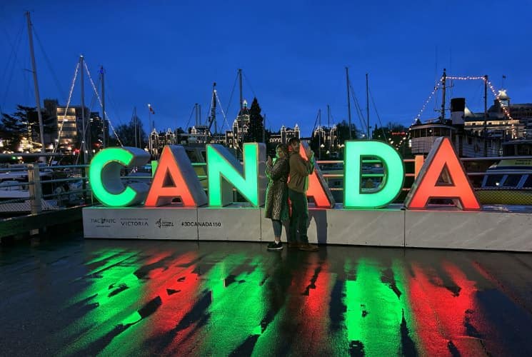 People standing in front of large Canada sign lighted with neon green and red lights