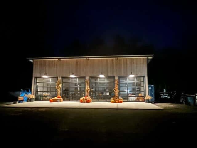 A wood building with 4 glass garage doors and pumpkins and hay bales in front