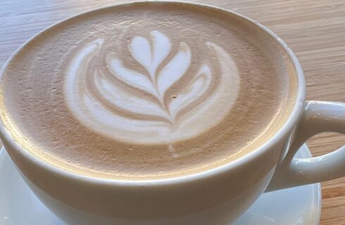 Close up view of a white coffee cup filled with a coffee drink with white decoration in the foam