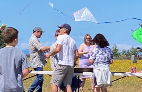 People standing near a white table in a field of flowers getting ready to fly kites