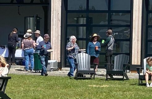 People attending an event standing, talking, and sitting in Adirondack chairs on green grass