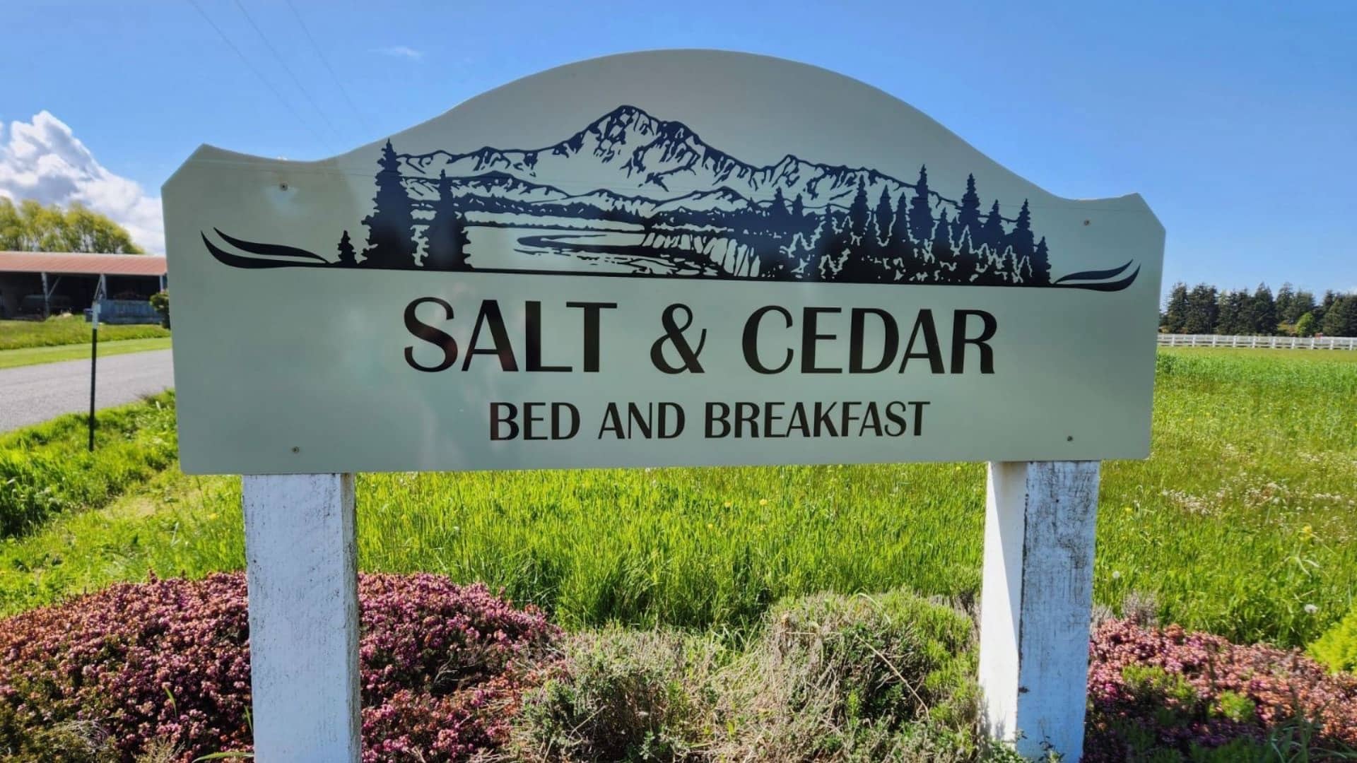 Sign showing Salt & Cedar Bed and Breakfast logo and text in a field of green grass