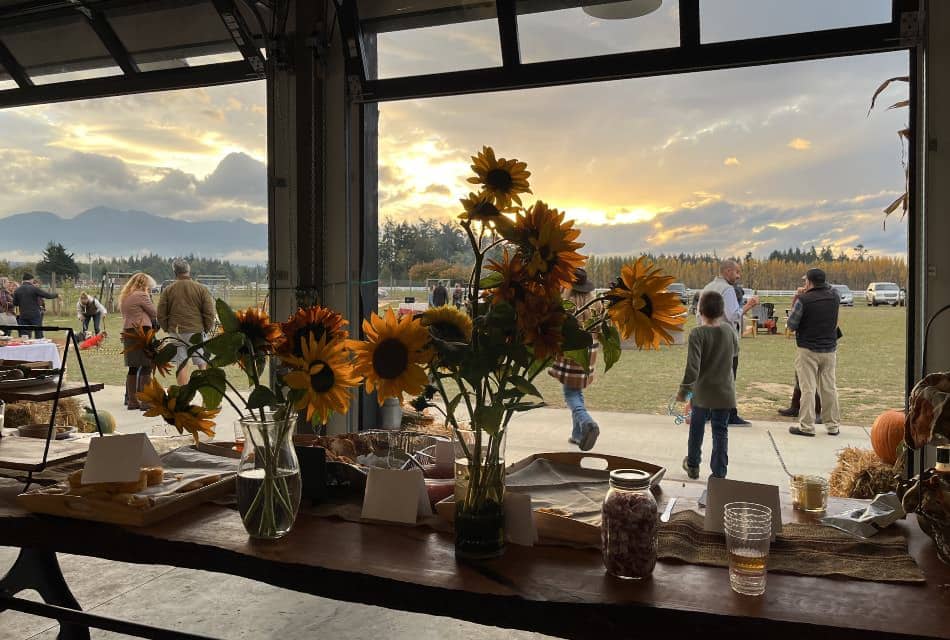 Event space with open garage doors, large wooden table covered with flower vases and serving containers, and mountain and clouds in the background