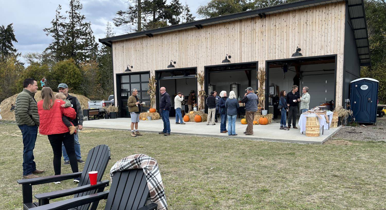 Cidery building with open garage doors set up for a fall inspired event with multiple people standing and visiting together