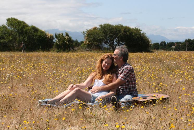 Man kissing woman's head sitting in a field of yellow flowers